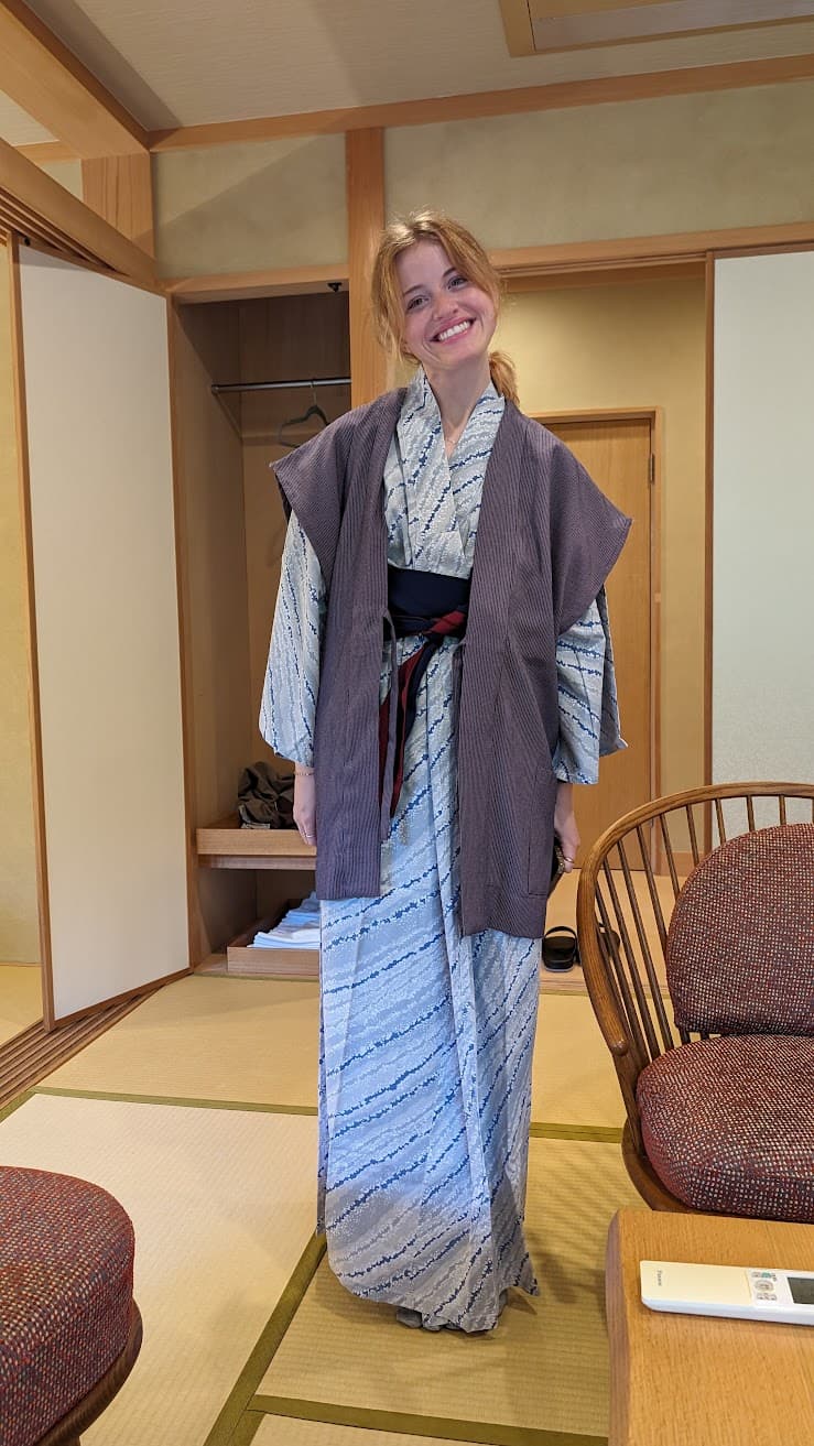 In a quiet tatami room where pale wood frames the hush, an artist pauses between journeys, wrapped in borrowed patterns that whisper of old roads and slow evenings. Light pools softly on the floor as if time has decided to sit down too, holding space for a smile that feels both grateful and unhurried. The moment hums with calm—a small sanctuary where travel becomes tenderness and inspiration breathes.